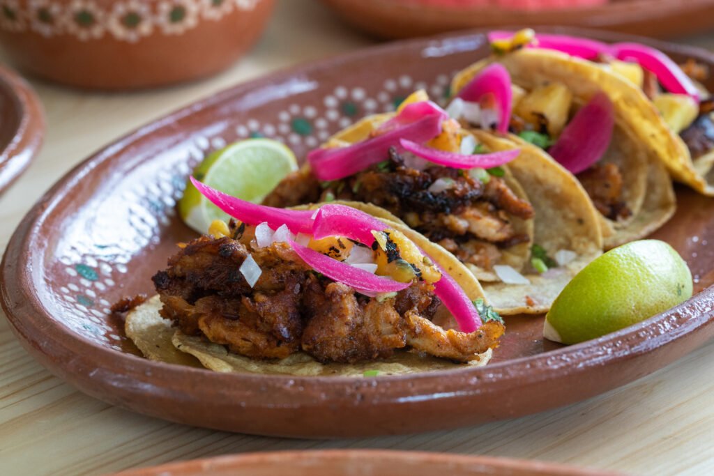 Close-up of flavorful Mexican tacos al pastor on a plate, made with marinated pork, fresh onions, and cilantro — a classic dish from traditional Mexican cuisine.