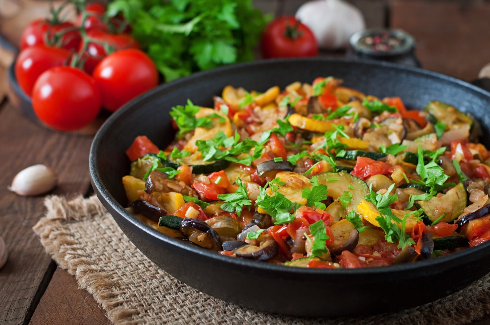 Top view of colorful vegetable ratatouille in a frying pan on a rustic wooden table — a healthy and flavorful dish from French cuisine.