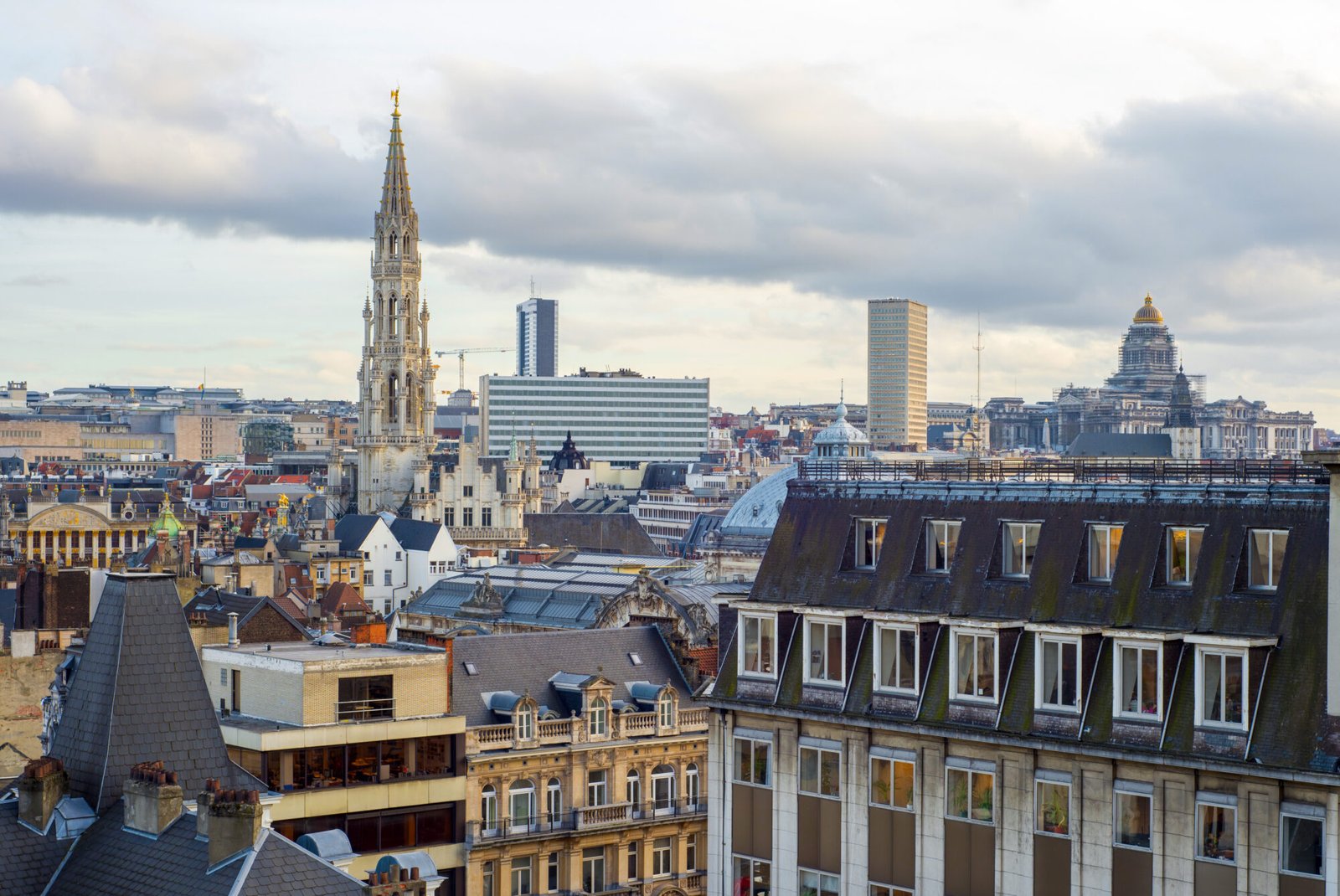 Panoramic view of Brussels, Belgium, featuring the Gothic-style spire of the Town Hall, modern buildings, and the domed Palace of Justice in the background.