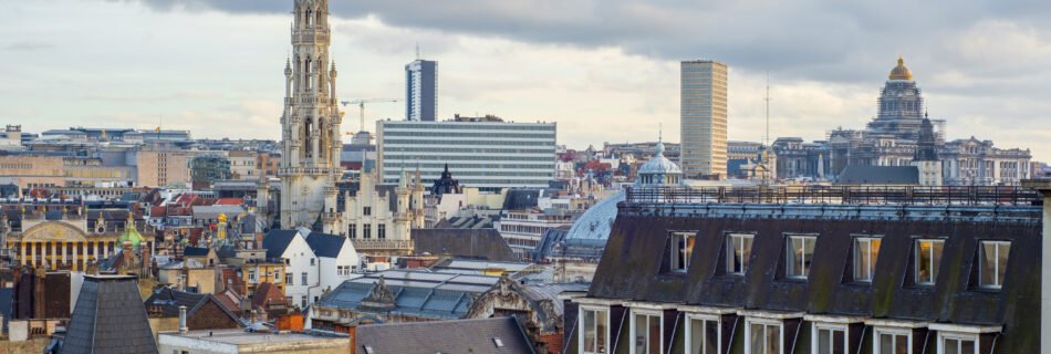 Panoramic view of Brussels, Belgium, featuring the Gothic-style spire of the Town Hall, modern buildings, and the domed Palace of Justice in the background.