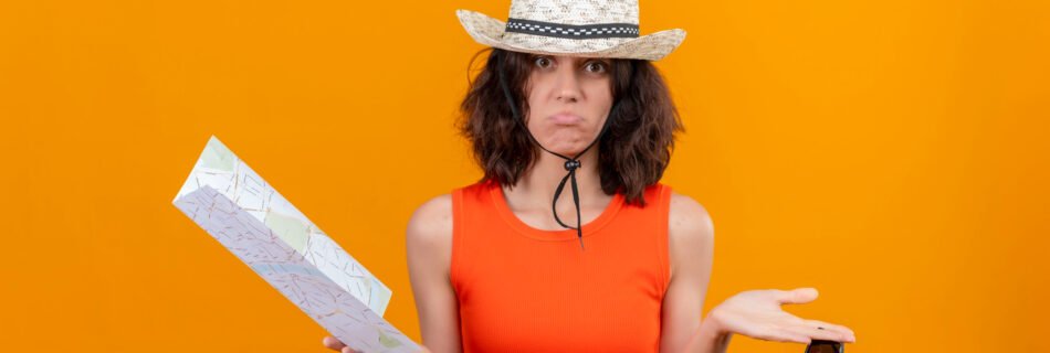 Frustrated female traveler in an orange dress and straw hat holding a map in one hand and sunglasses in the other, looking confused against an orange background — representing travel mistakes or getting lost on a trip.
