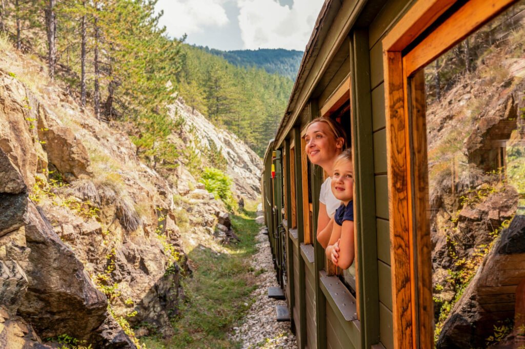Mother and her child looking out the window of a train on a sunny day while traveling through Europe, enjoying the scenic landscape.