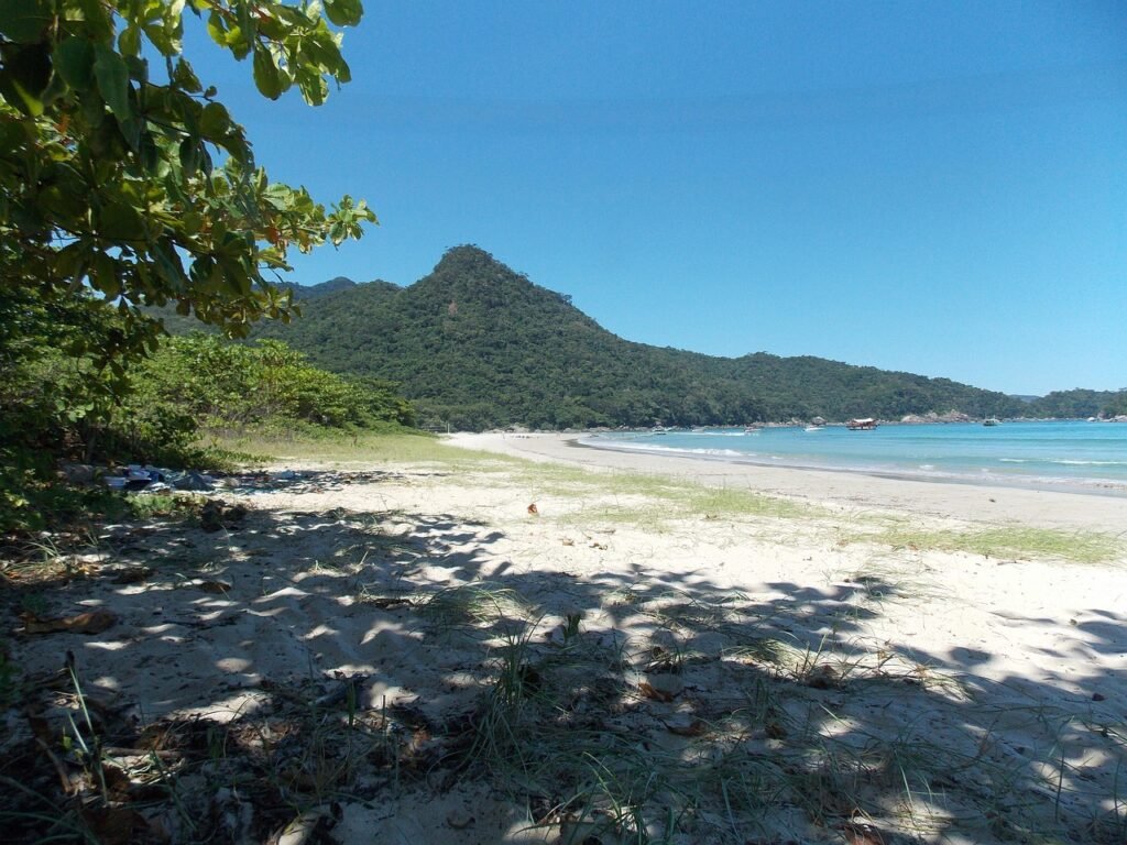 Tropical beach in Ilha Grande, Brazil, with lush green mountains, golden sand, and boats floating on clear blue water.