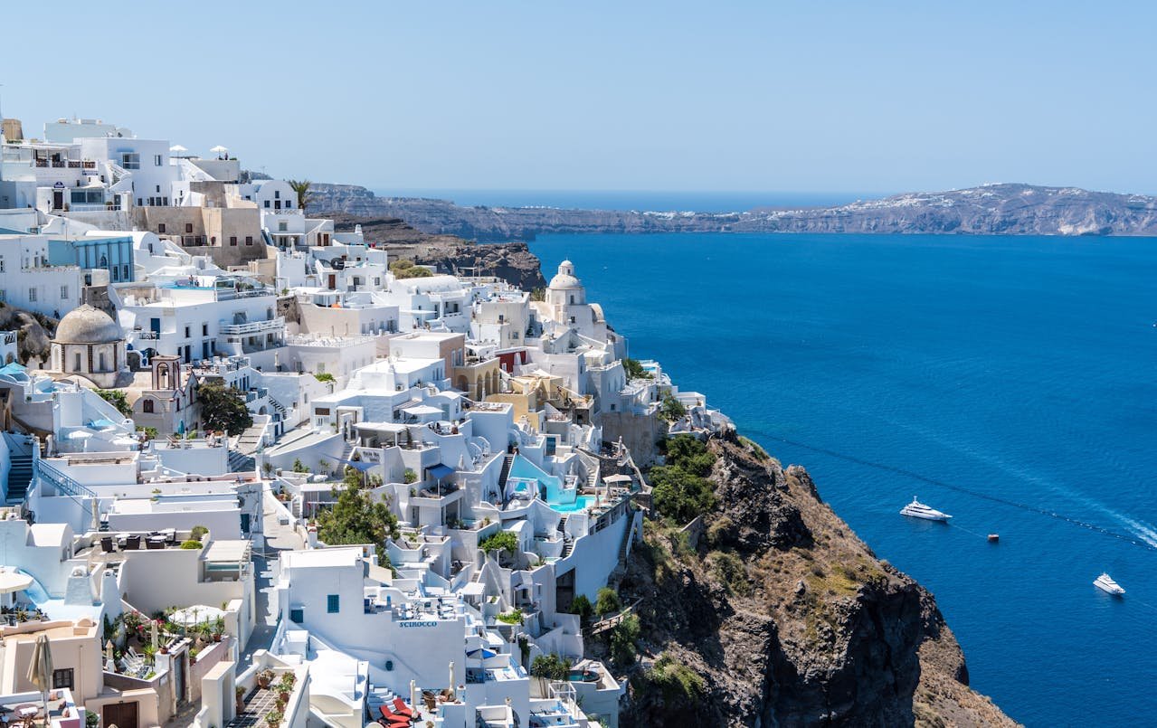 Panoramic view of Santorini, Greece, featuring iconic white houses on cliffs facing the deep blue sea under a partially cloudy sky.