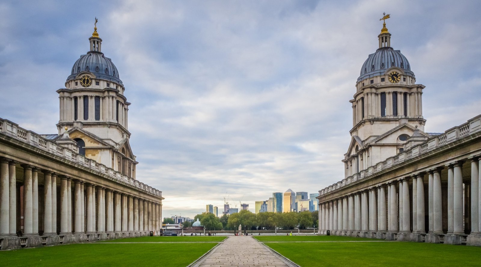 Historic buildings of the Old Royal Naval College in Greenwich, London 🇬🇧, with classical architecture and a view of Canary Wharf skyline in the background — a perfect blend of heritage and modernity in one of the most beautiful cities in England.